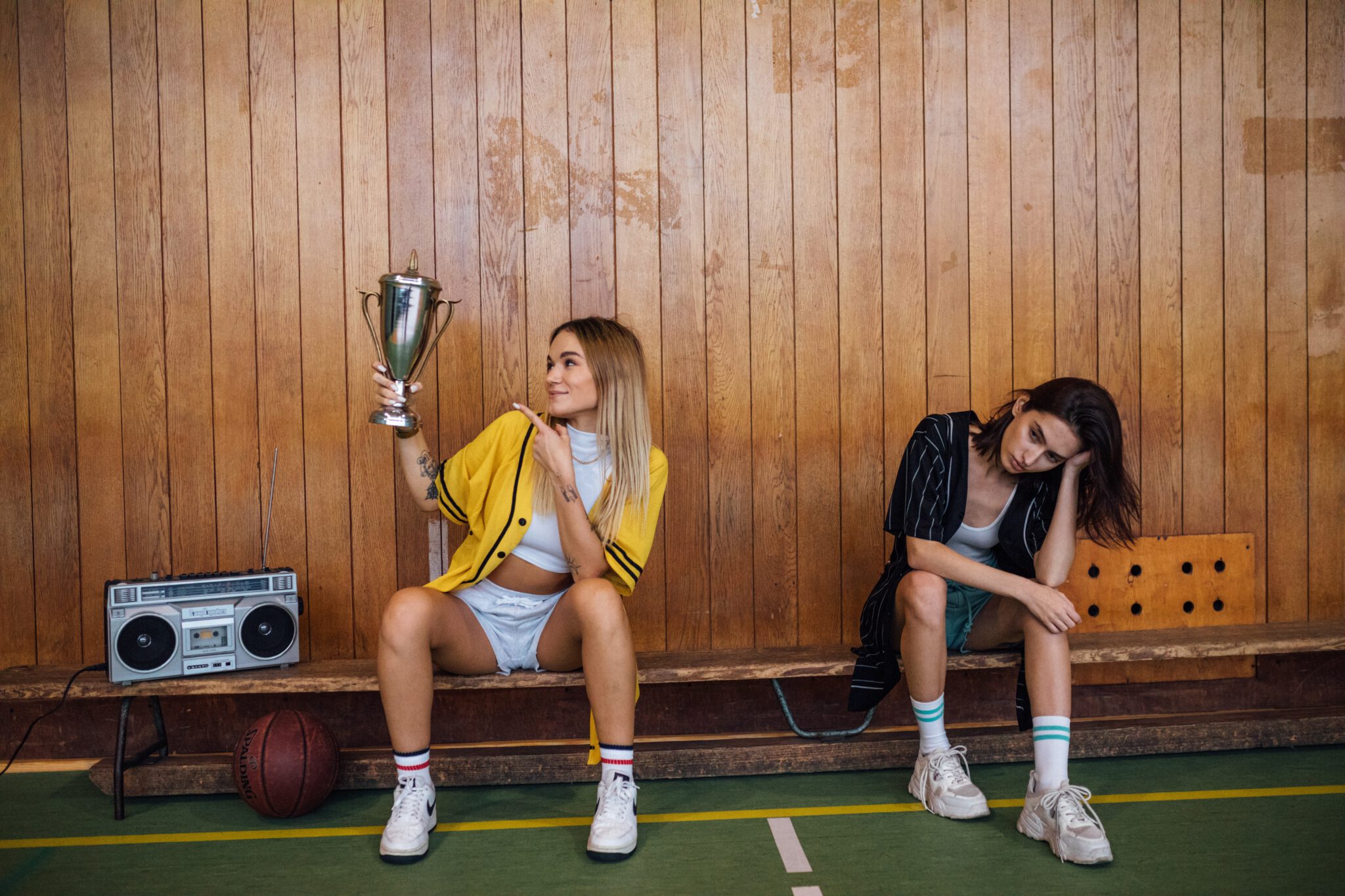 twee vrouwen op een bankje terwijl een overwinningsbeker vast heeft en de ander somber kijkt en bedenkt waarom je jezelf niet moet vergelijken met anderen